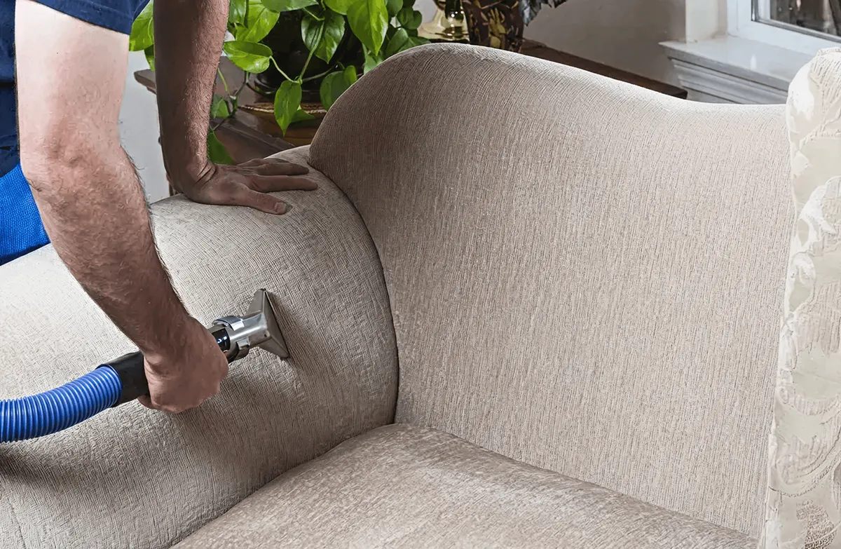 Professional upholstery cleaner deep-cleaning a fabric sofa with a handheld extraction tool and hose, Las Vegas, NV.